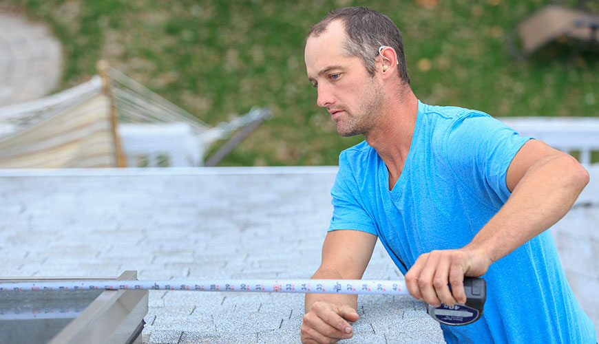 A Caucasian man  is using a measuring tape on a construction site. He is wearing hearing aids.