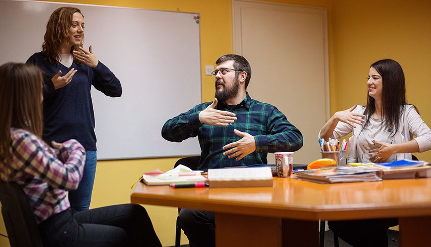 A group of men and women are in a staff meeting. They are all communicating  together through sign language.