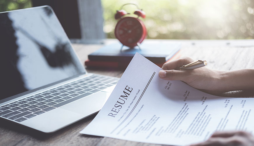 A close-up of a resume on a desk. with a laptop in the background. 