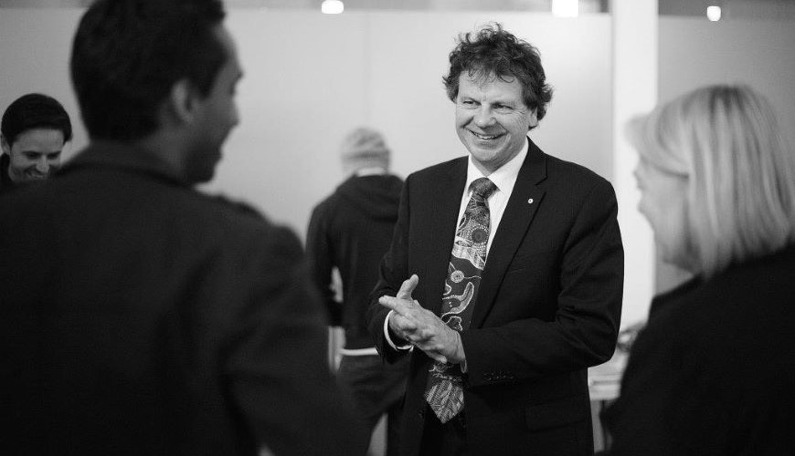 Black and white image of Simon speaking with others. He is wearing a suit