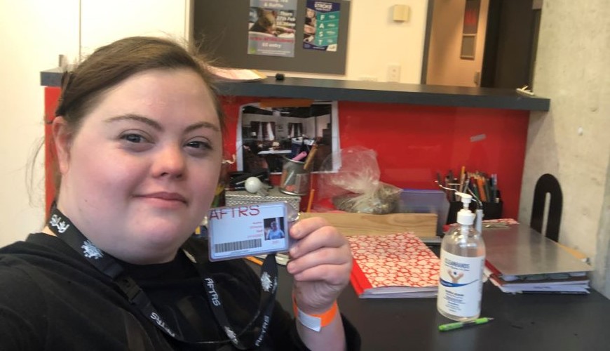 Image of Audrey sitting at her desk taking a selfie holding up her AFTRS employee card 