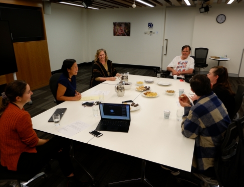 A group of people sitting around a white table engaged in conversation. 