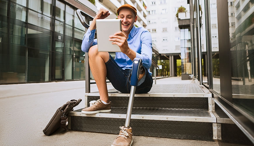 A man sitting on a step speaking on a tablet. He has a prosthetic leg.