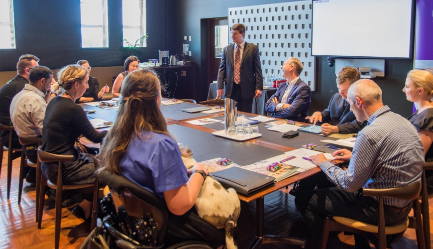 Image of Paul presenting to a group of people sitting at a table 