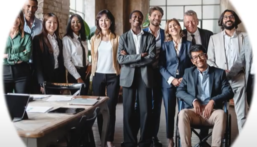 Image of a group of people wearing office attire and standing in a warehouse. One man is in a wheelchair