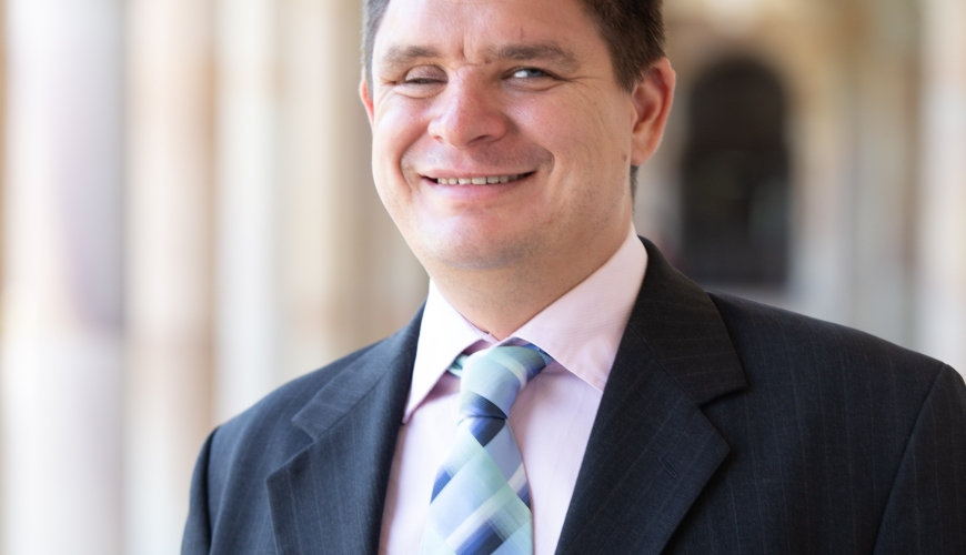 Image of Paul wearing a suit and tie and smiling at the camera