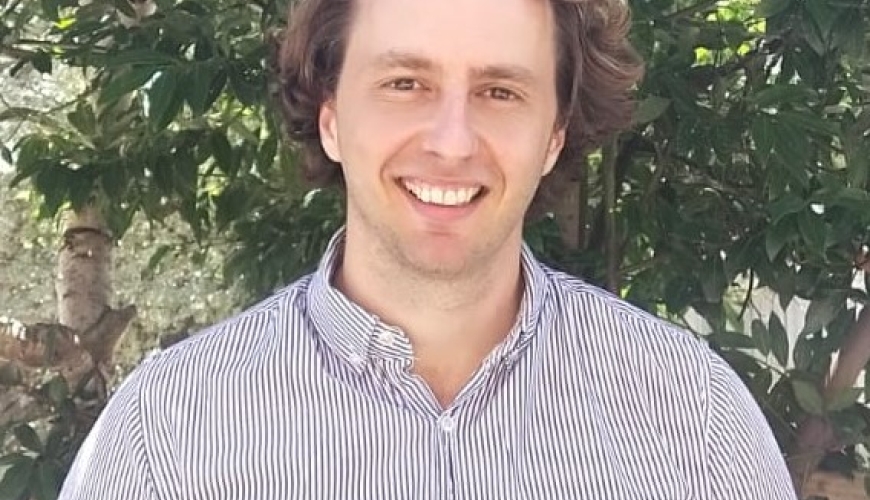 Image of Simon wearing a shirt and standing in front of a tree. Simon is smiling