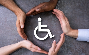 A group of hands, all with different coloured skin tones, create a circle around a sign for disability.